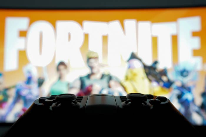 Person holding a game controller with the video game Fortnite on screen showcasing characters