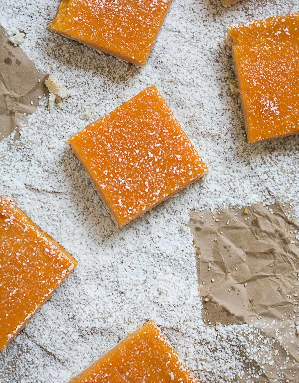 Square-shaped papaya bars dusted with powdered sugar on a flecked surface with parchment paper