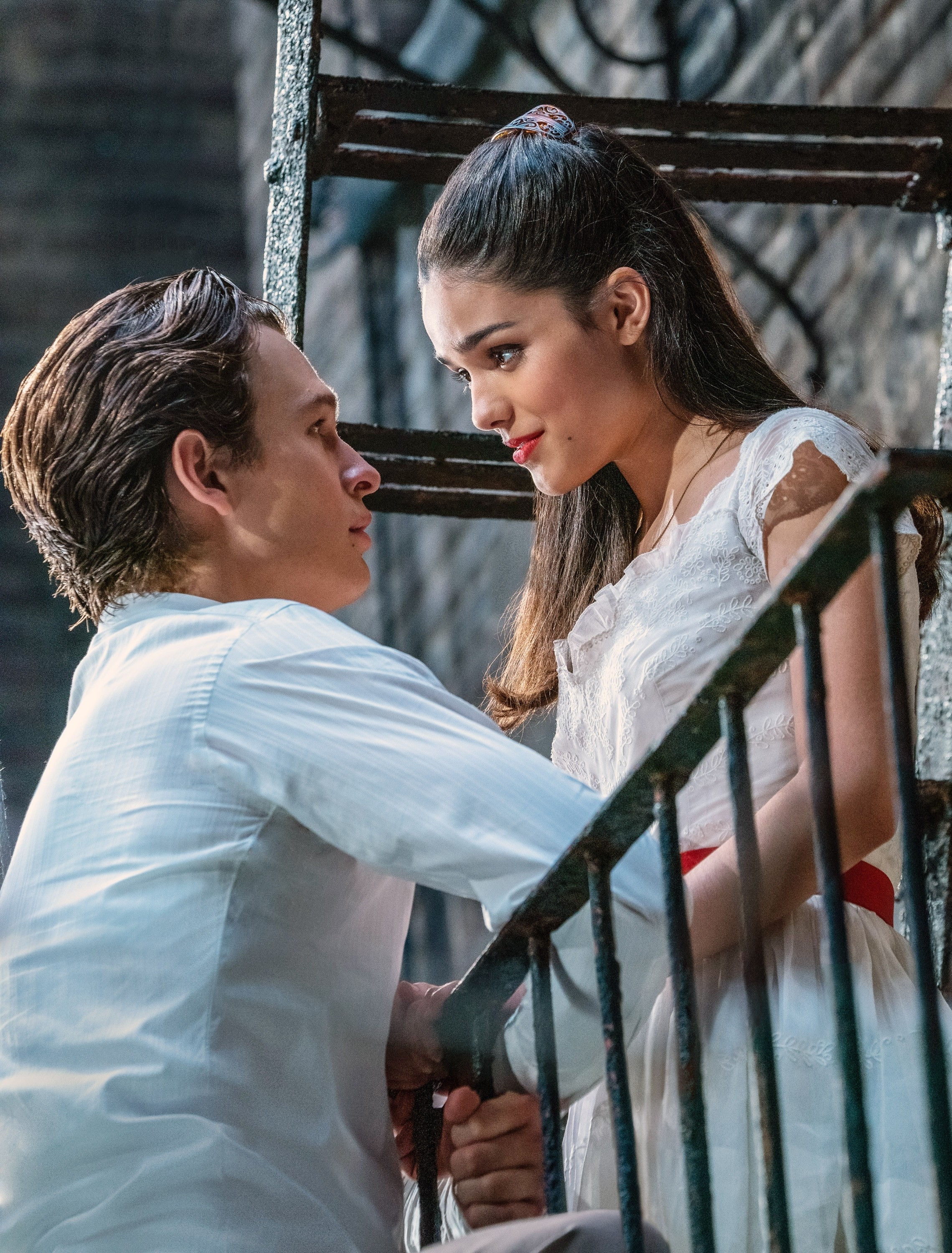 Tony and Maria from West Side Story gaze into each other&#x27;s eyes on a fire escape. Maria wears a white dress and Tony, a white shirt
