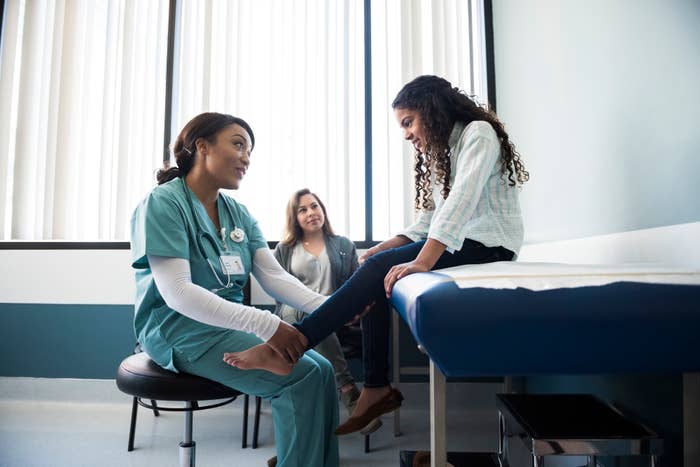 A healthcare professional is examining a child's knee in a medical office while another professional observes