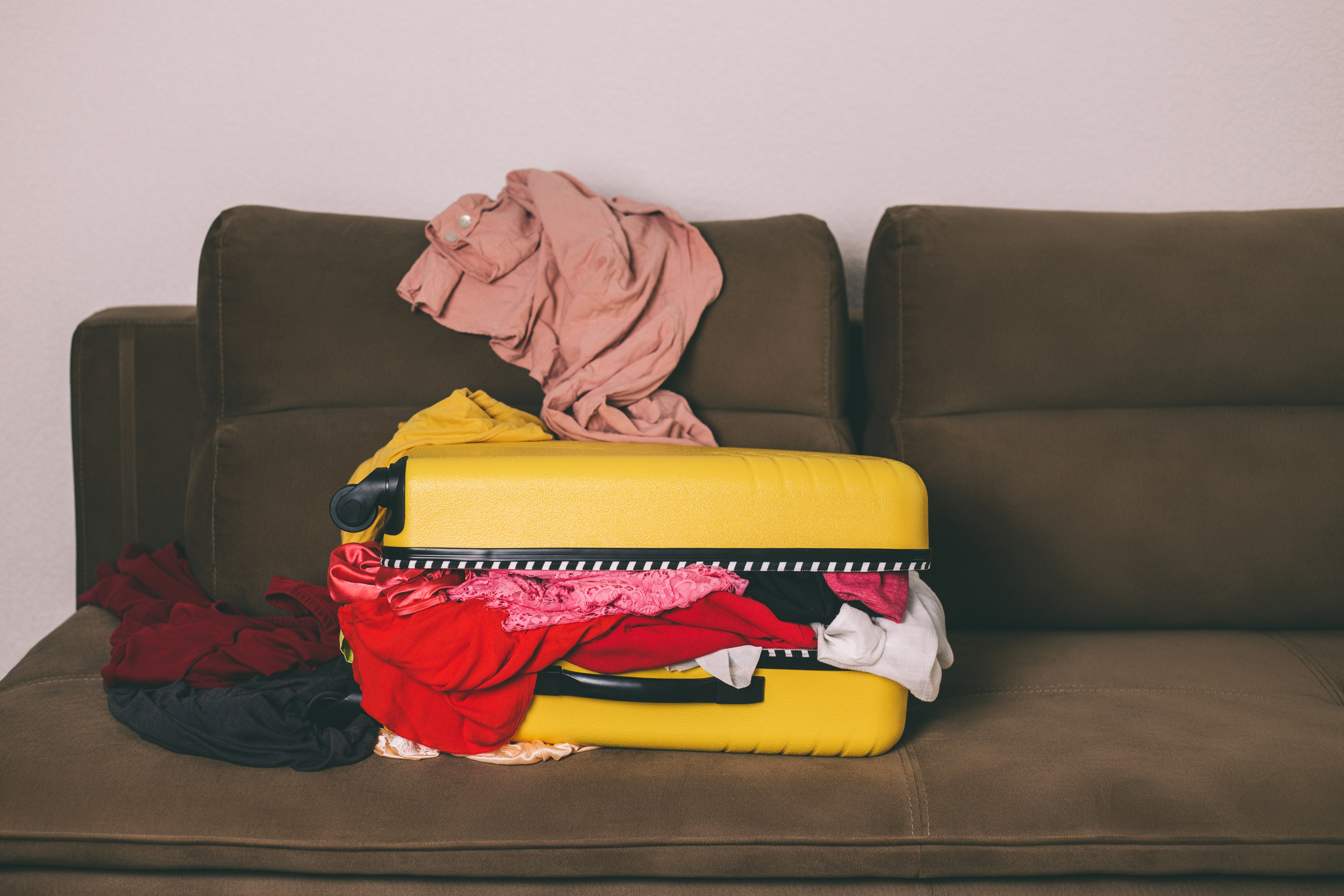 Overpacked yellow suitcase with clothes on a sofa, suggesting travel preparation challenges