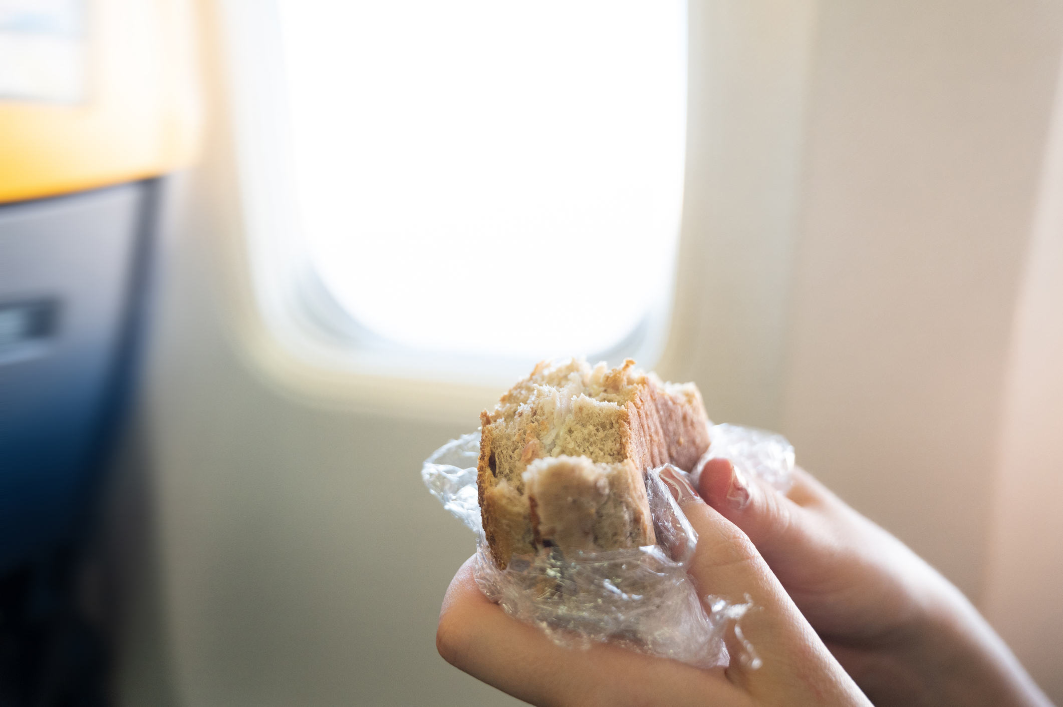 Person holding a sandwich with airplane window in the background, illustrating in-flight meal