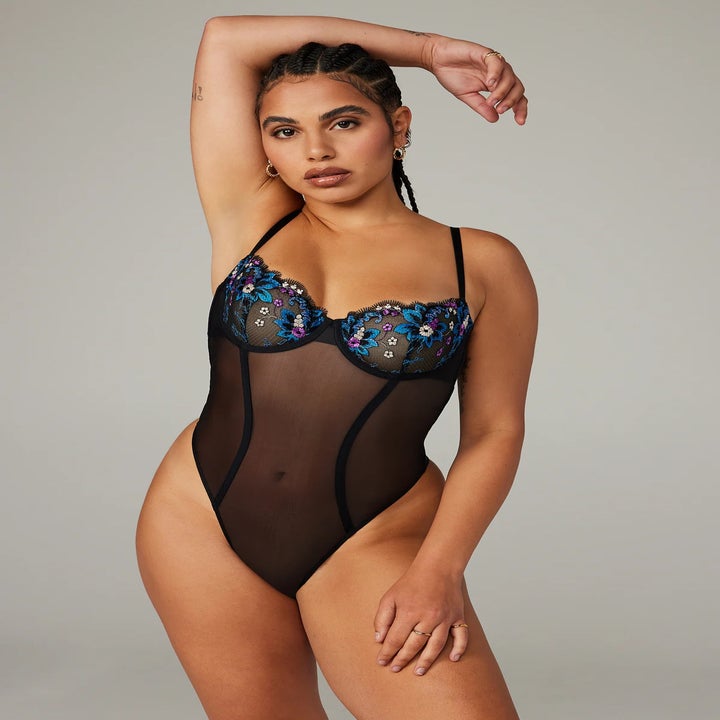 A person posing in a sheer bodysuit with embroidered details
