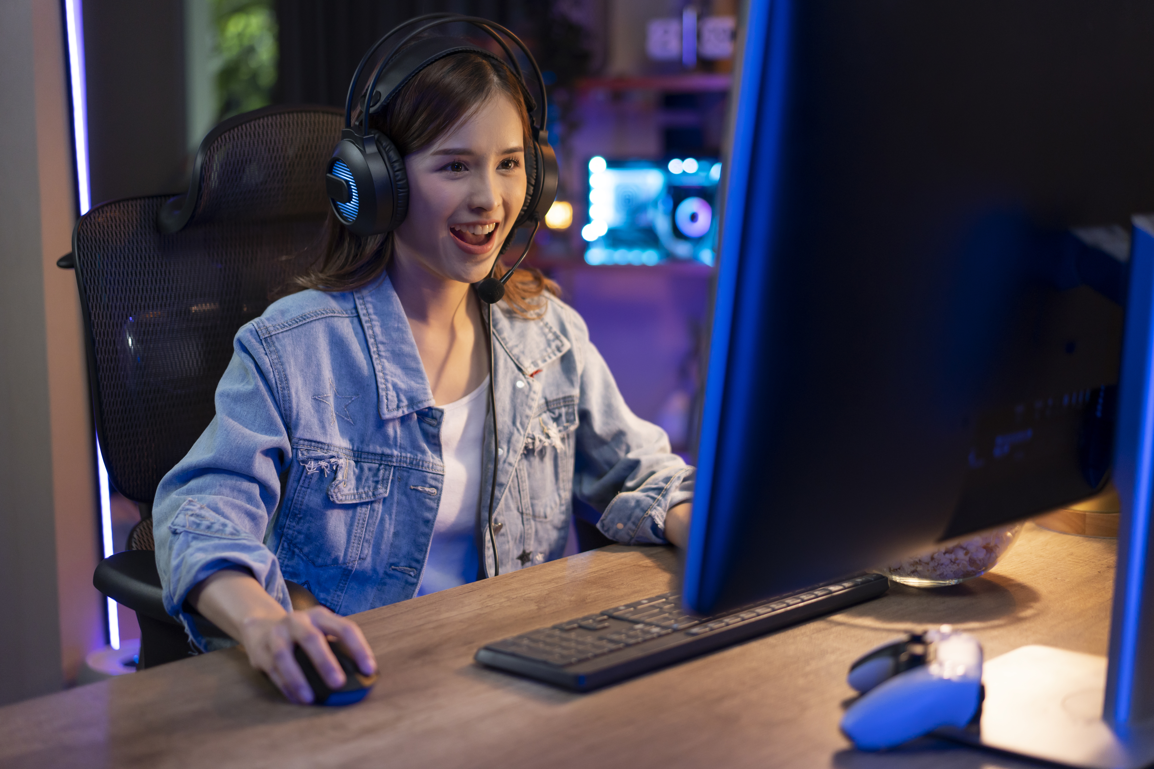 Woman in headset at computer desk with screen, smiling, possibly engaging in remote work or gaming