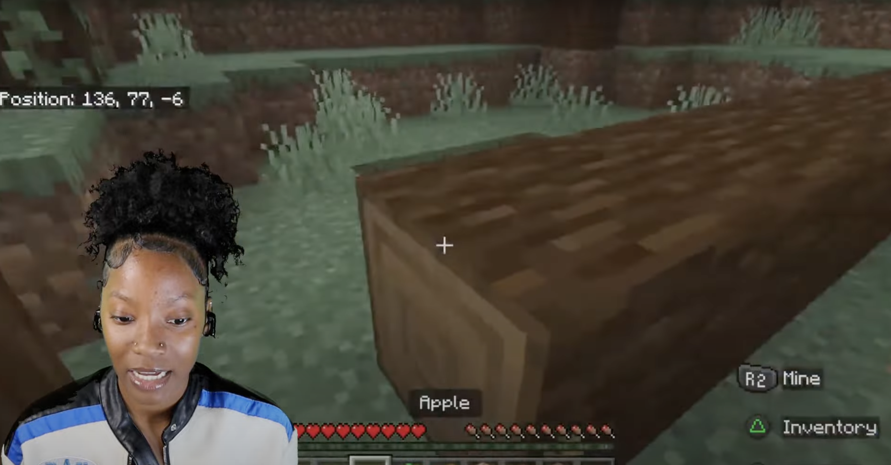Person playing Minecraft, showing inventory with an apple, overlaying gameplay scene