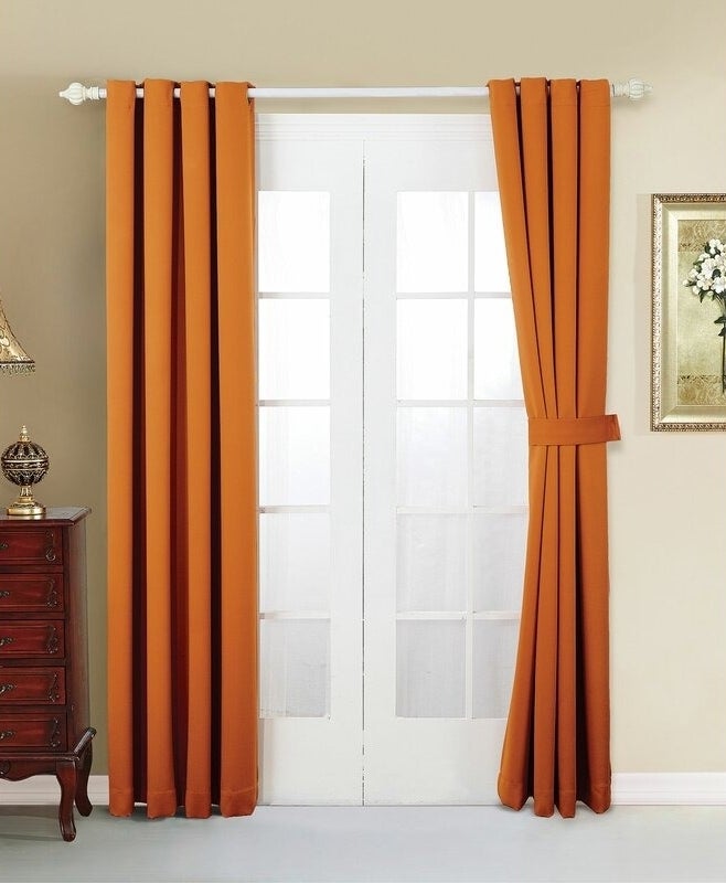 A set of orange curtains tied back on a window