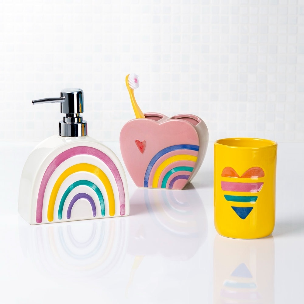 Bathroom set with rainbow motifs, including a soap dispenser, toothbrush holder, and cup