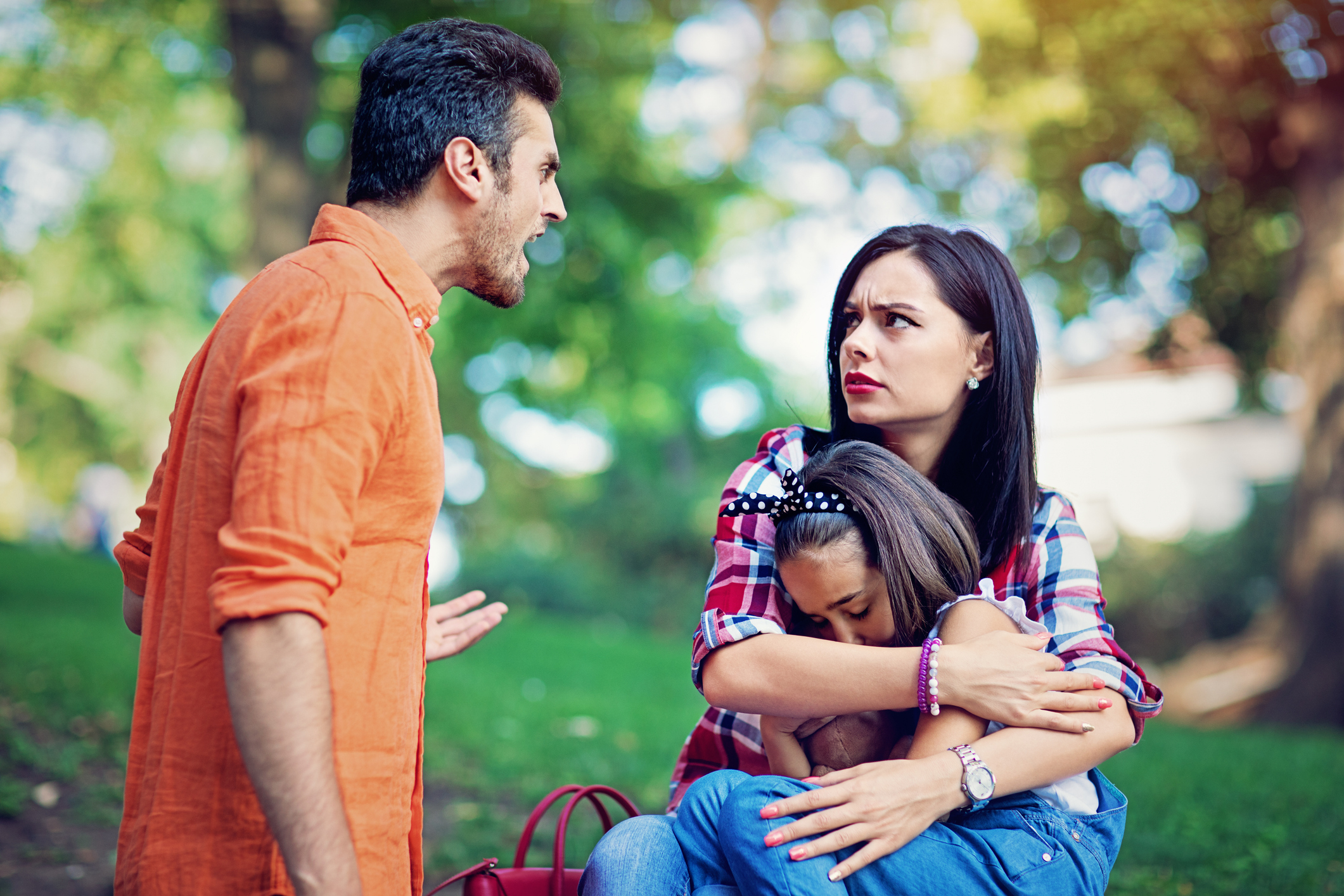 A man and woman having a disagreement while a young girl hugs the woman&#x27;s leg, outdoors