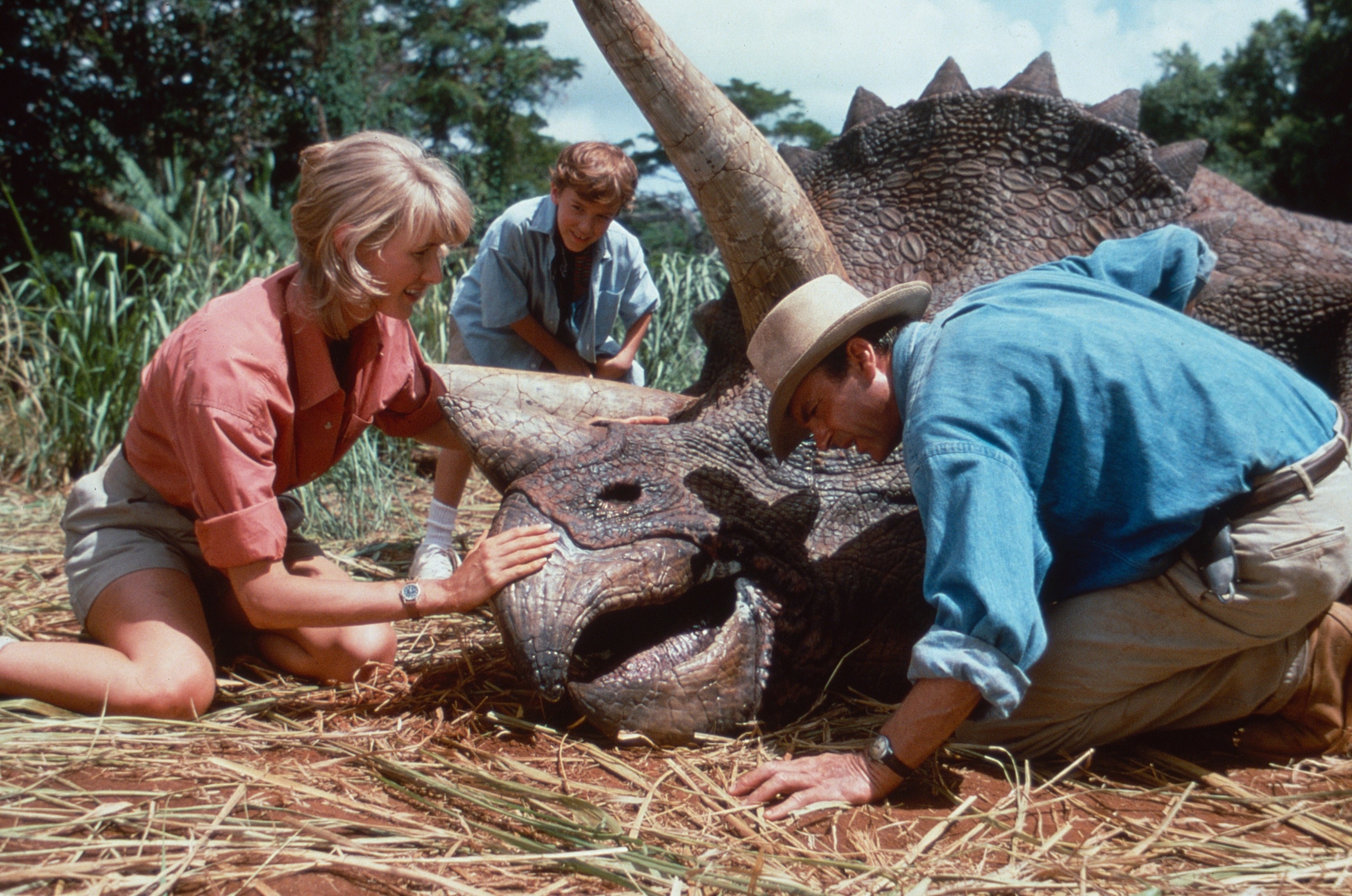 Three individuals, including characters Dr. Ellie Sattler and Dr. Alan Grant, attending to a sick Triceratops in a scene from Jurassic Park