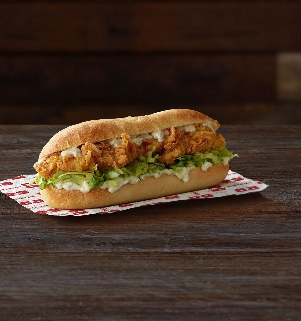 A chicken sandwich with lettuce and sauce on a bun, placed on a checkered wrapper atop a wooden surface