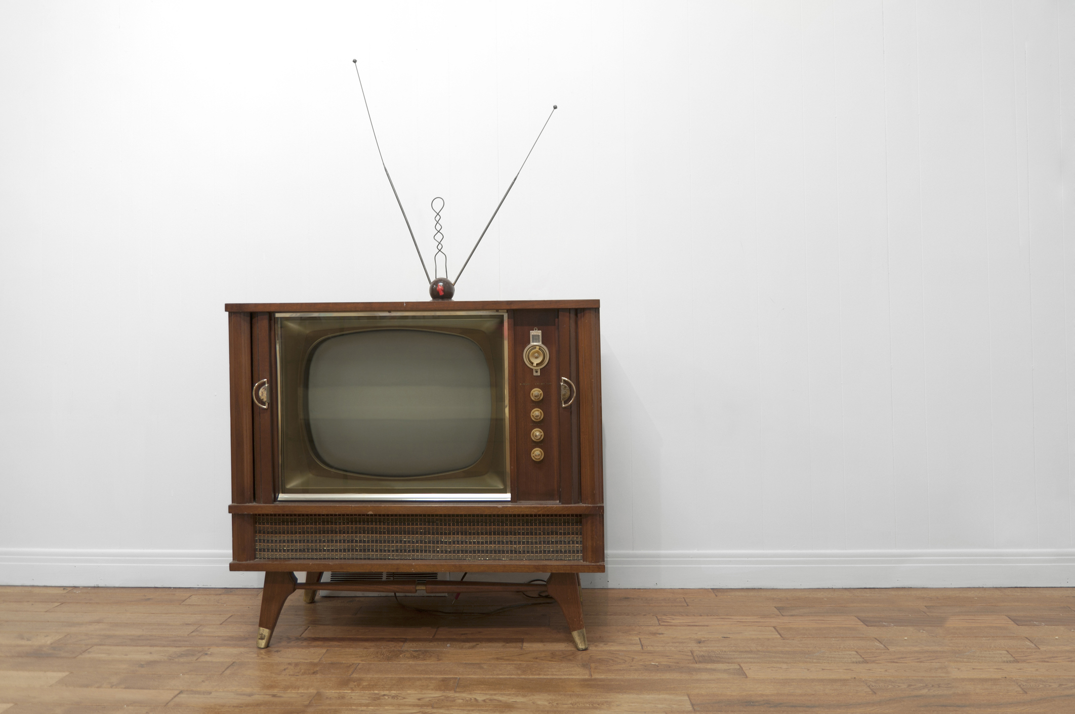 Vintage television with rabbit-ear antenna on a wood floor against a plain wall