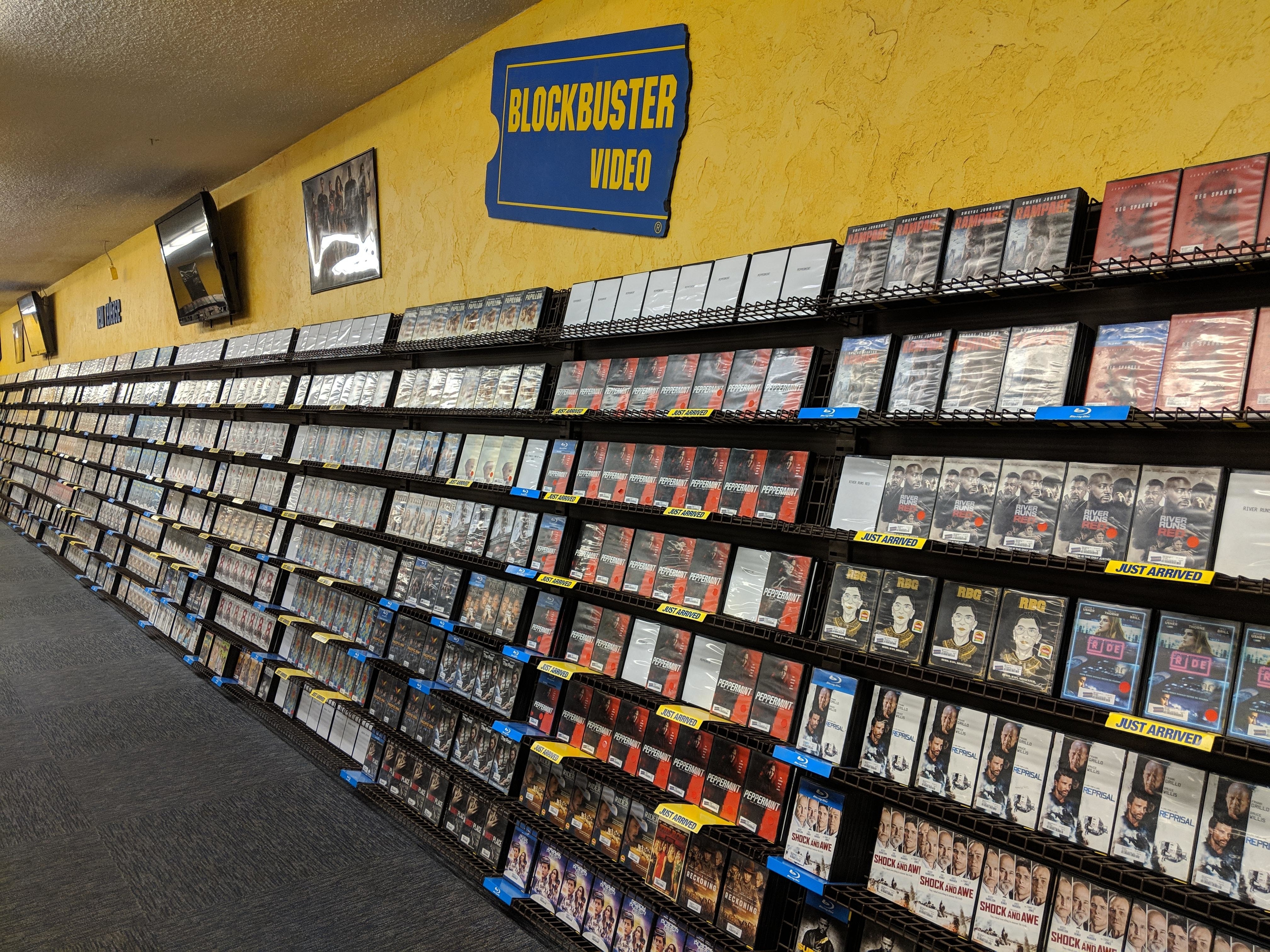 A Blockbuster Video store interior with shelves of DVDs and a distinctive sign above
