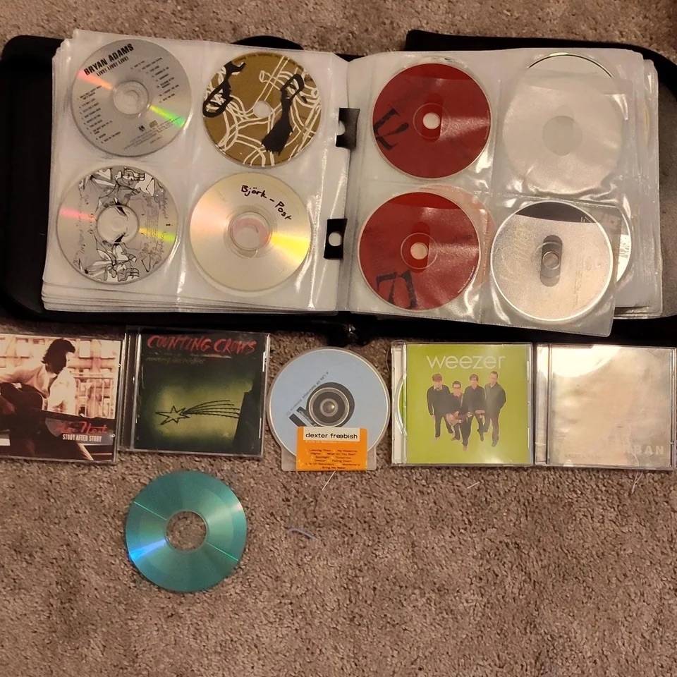 Compilation of various CDs including Weezer in a binder, evoking late &#x27;90s to early 2000s music nostalgia
