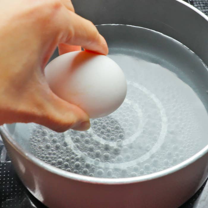 手が鍋に入れる卵を持っている。