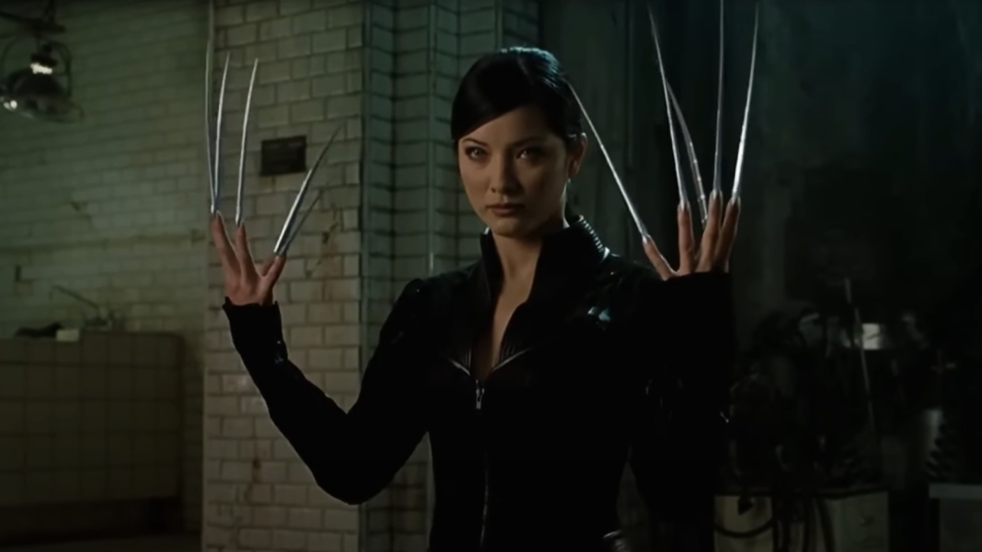Character with metal claws extended from each hand, wearing a black outfit, standing in a dimly lit room