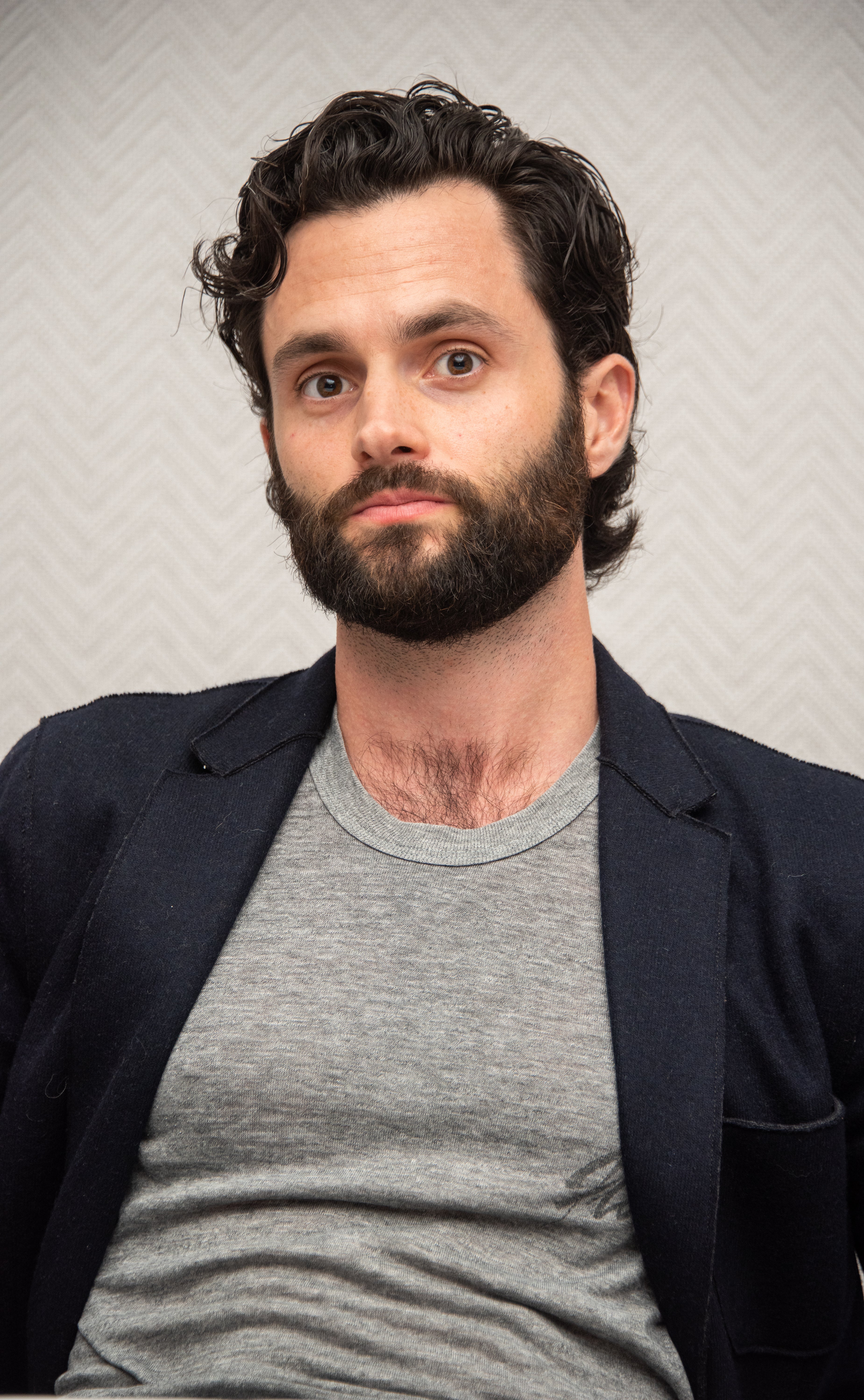 Penn with beard and curly hair wearing a blazer over a T-shirt, seated and looking at the camera