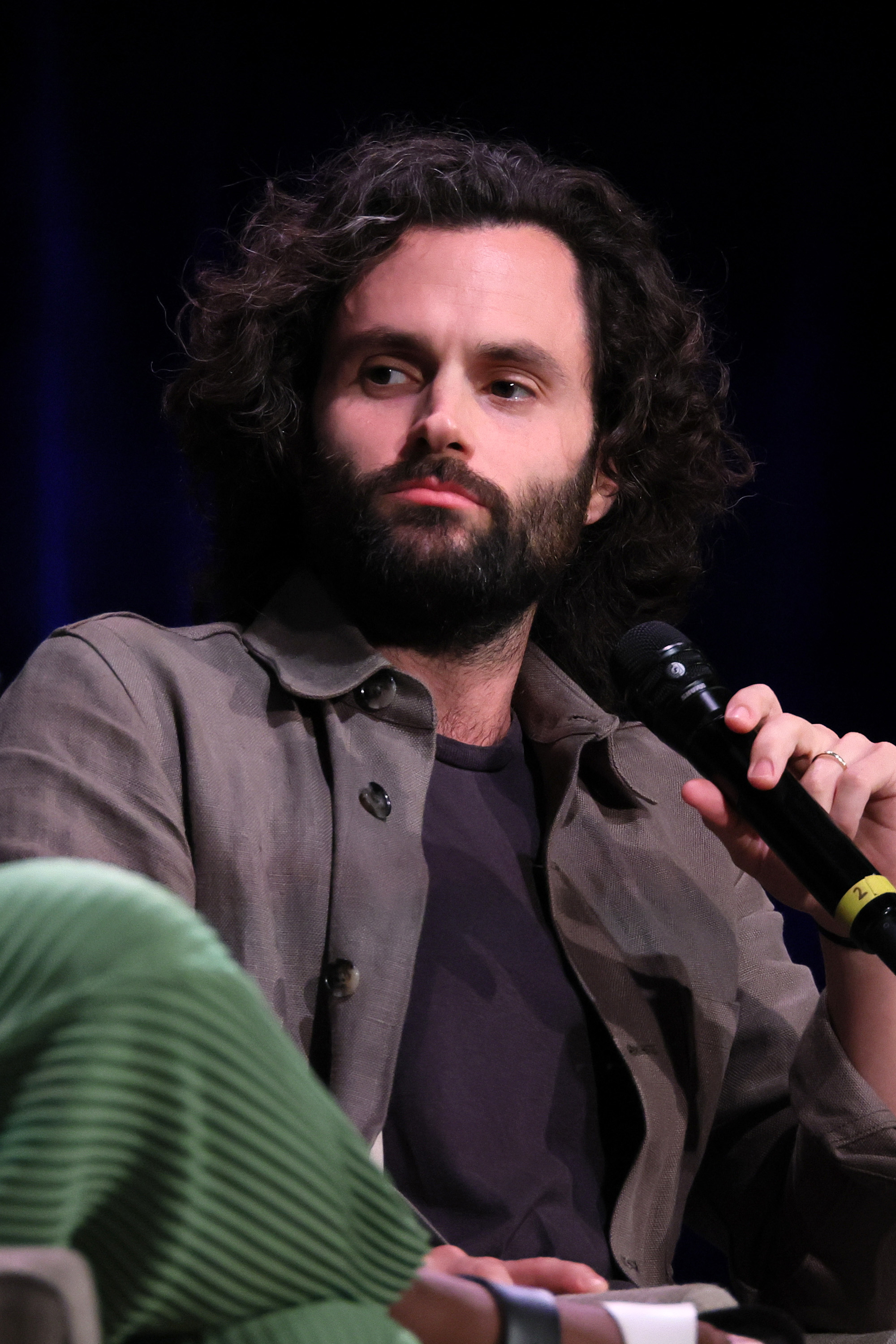 Penn holding a microphone, wearing a buttoned shirt, sitting at a panel
