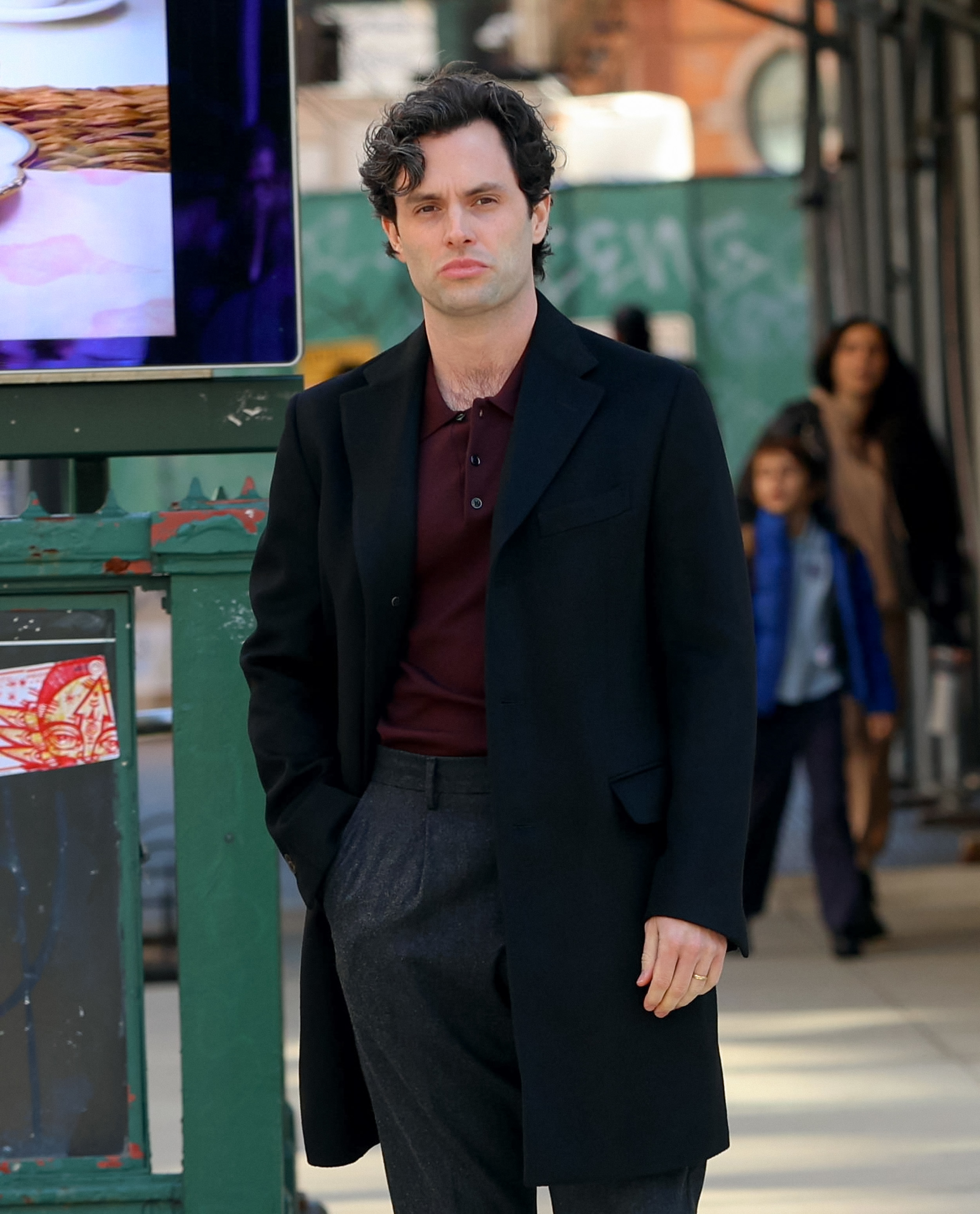 Penn in a black coat and gray trousers walking on a sidewalk