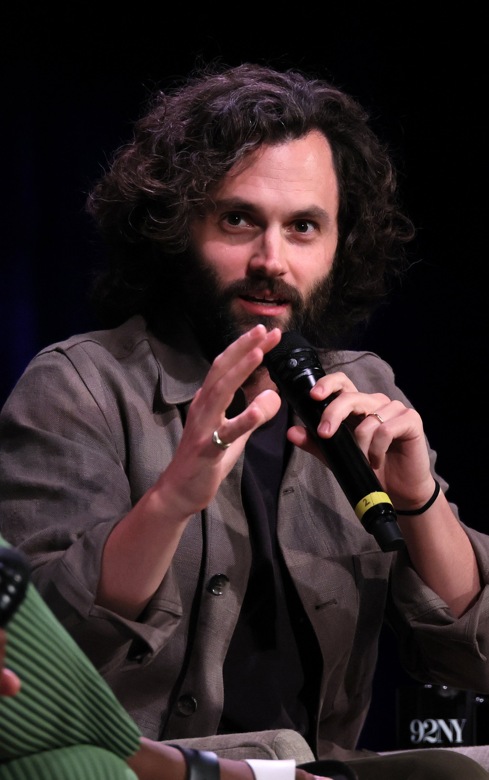 Penn speaking into a microphone, gesturing with his hands, wearing a casual jacket