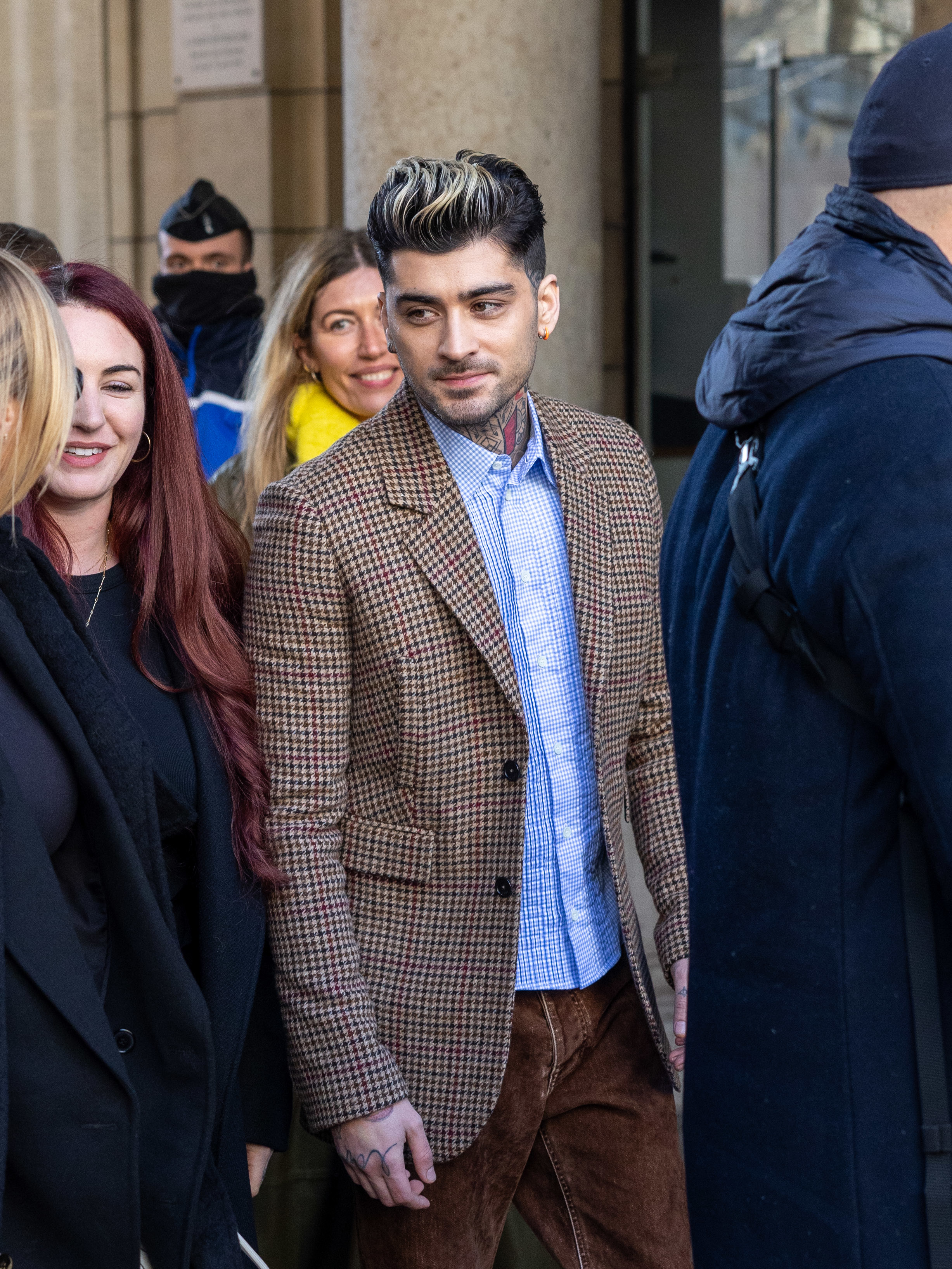 Zayn Malik in a checkered jacket and brown trousers in a group of people
