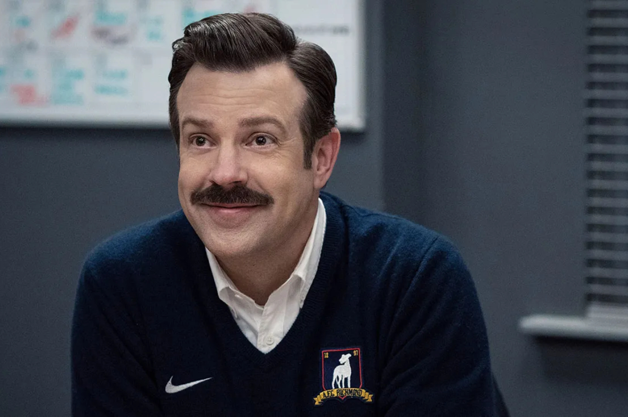 Jason Sudeikis as Ted Lasso, wearing a whistle, in a coach&#x27;s blue sweater with logo