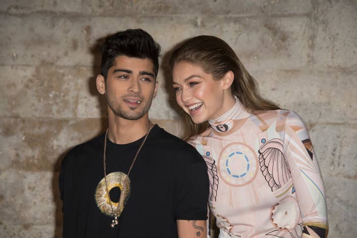 Zayn in a graphic print shirt and long necklace, and Gigi with a high-neck print outfit, both smiling