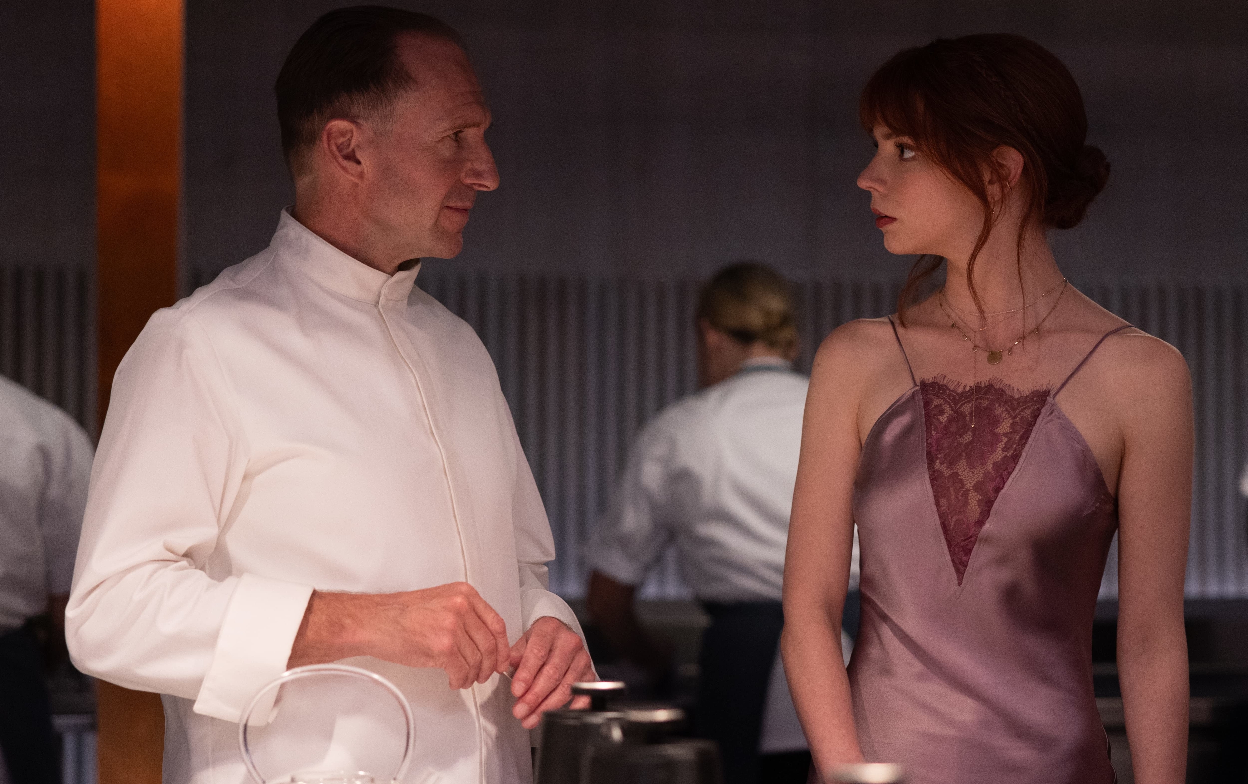 Two actors in a scene from a TV show or movie, man in a chef&#x27;s attire and woman in a formal dress, engaged in conversation