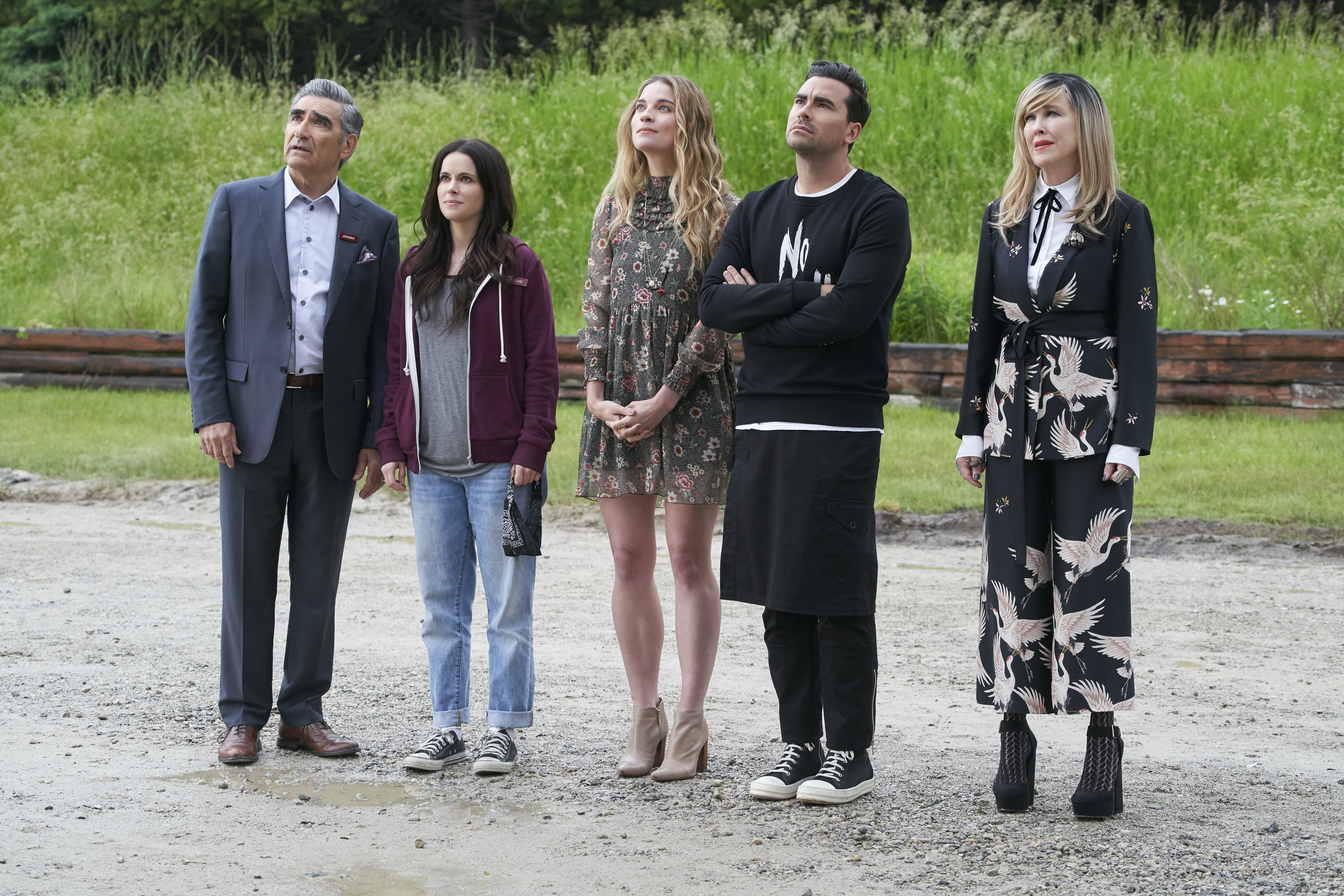 Five characters from Schitt&#x27;s Creek standing together, dressed in their distinctive styles, outdoors
