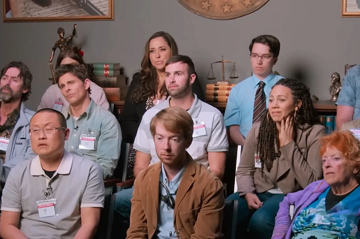 Group of people sitting in a courtroom gallery with attentive expressions, from a TV show scene