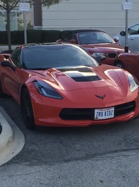 A red Corvette is parked in a spot designated for &#x27;Expecting Mothers&#x27; with a vanity plate reading &#x27;ZRO KIDZ&#x27;