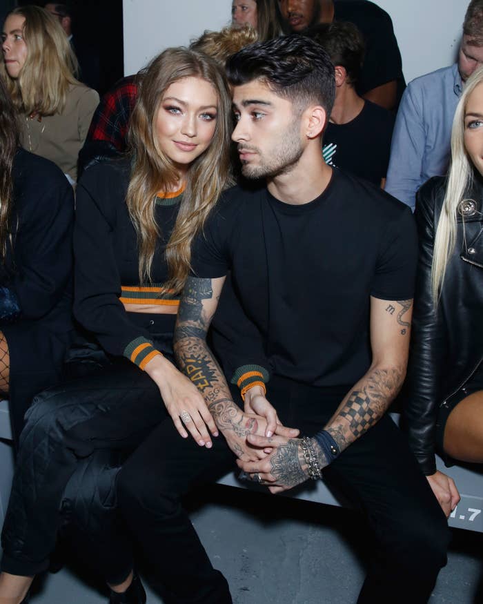 Gigi Hadid and Zayn Malik sitting side by side, Hadid in a black top with orange stripes, Malik in a plain black shirt