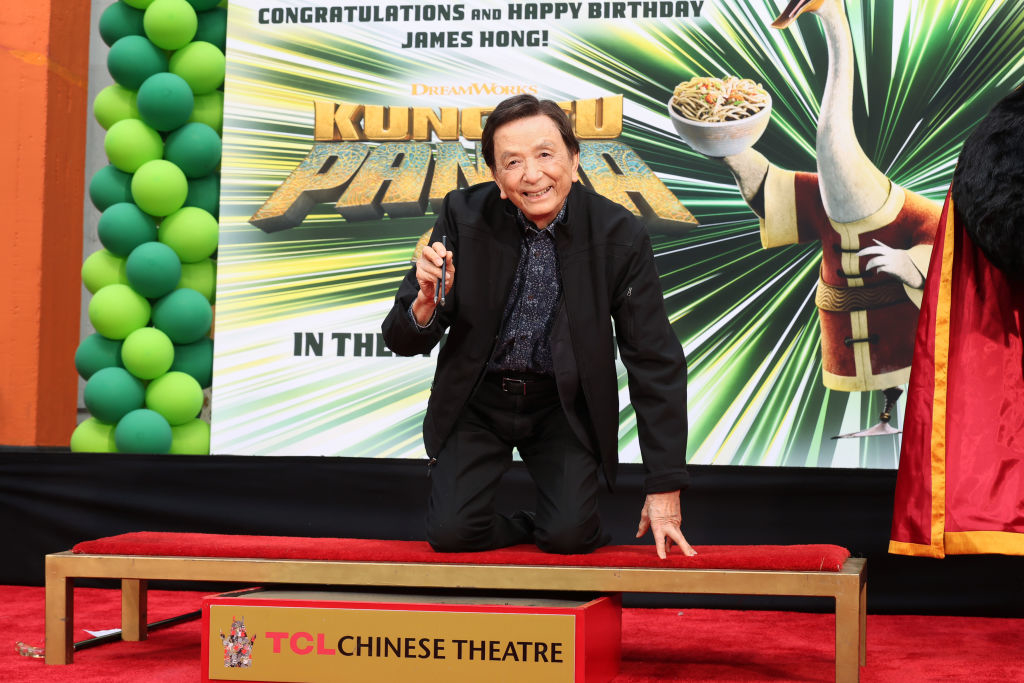 Man kneeling on red carpet at TCL Chinese Theatre with Kung Fu Panda poster; celebrating James Hong