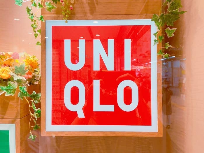 Red and white sign displaying &quot;UNIQLO&quot; on a store&#x27;s glass door with decorative greenery around it