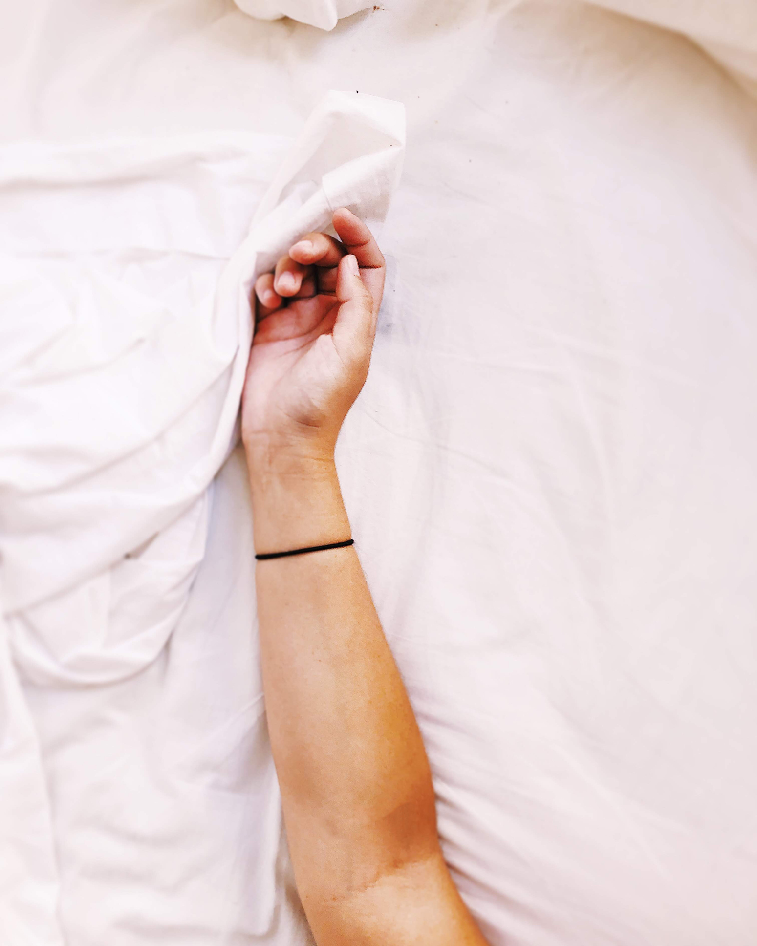 Person&#x27;s arm gripping a white sheet, partially covered, evoking a waking-up scene