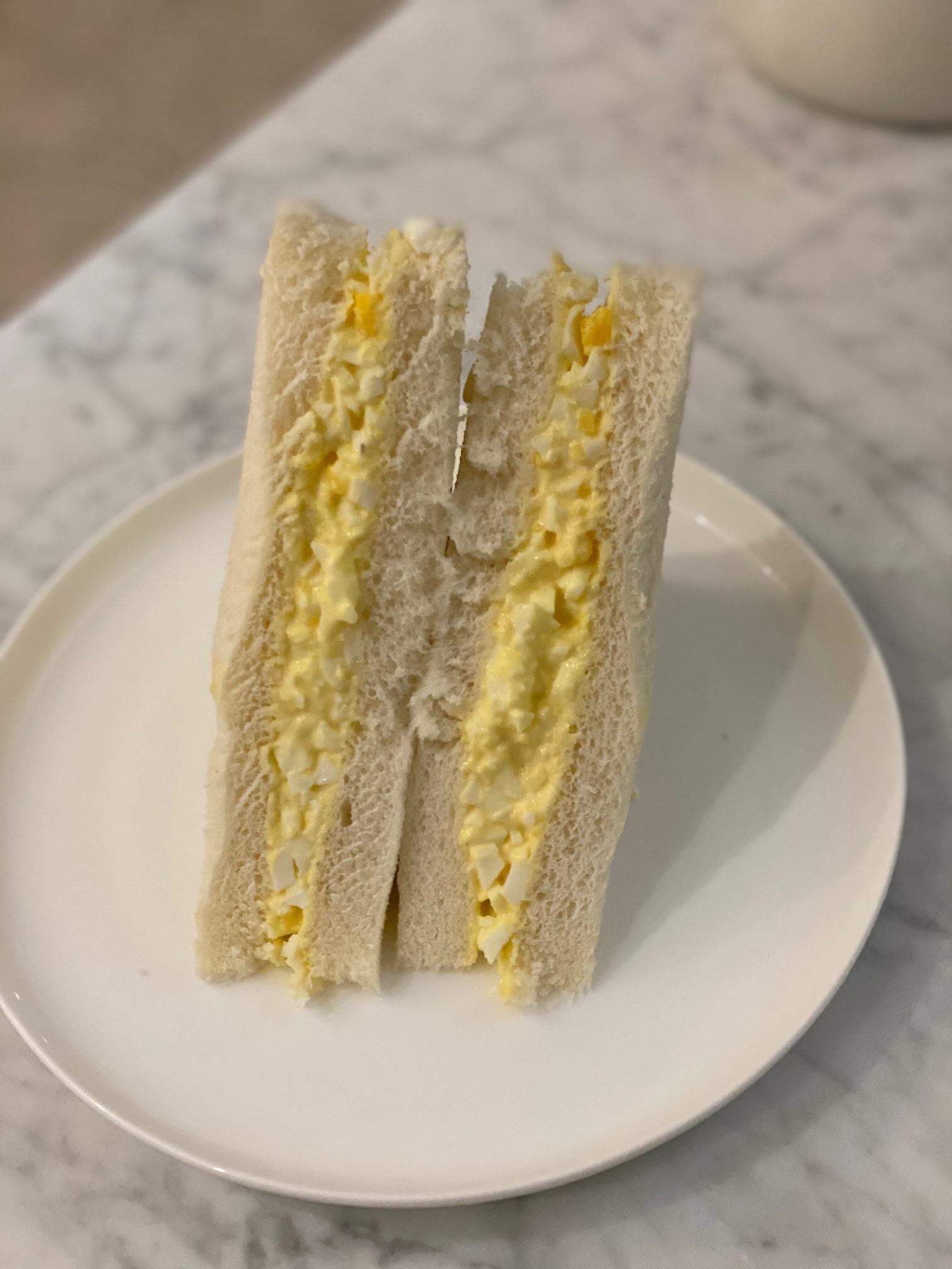 Egg salad sandwich with crusts removed, standing upright on a white plate