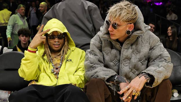 Two musicians sit side by side at an event, one in a bright yellow hoodie and the other in a patterned grey jacket