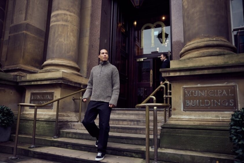 Man in casual sweater and trousers stands on steps outside a building with &#x27;MUNICIPAL BUILDINGS&#x27; sign