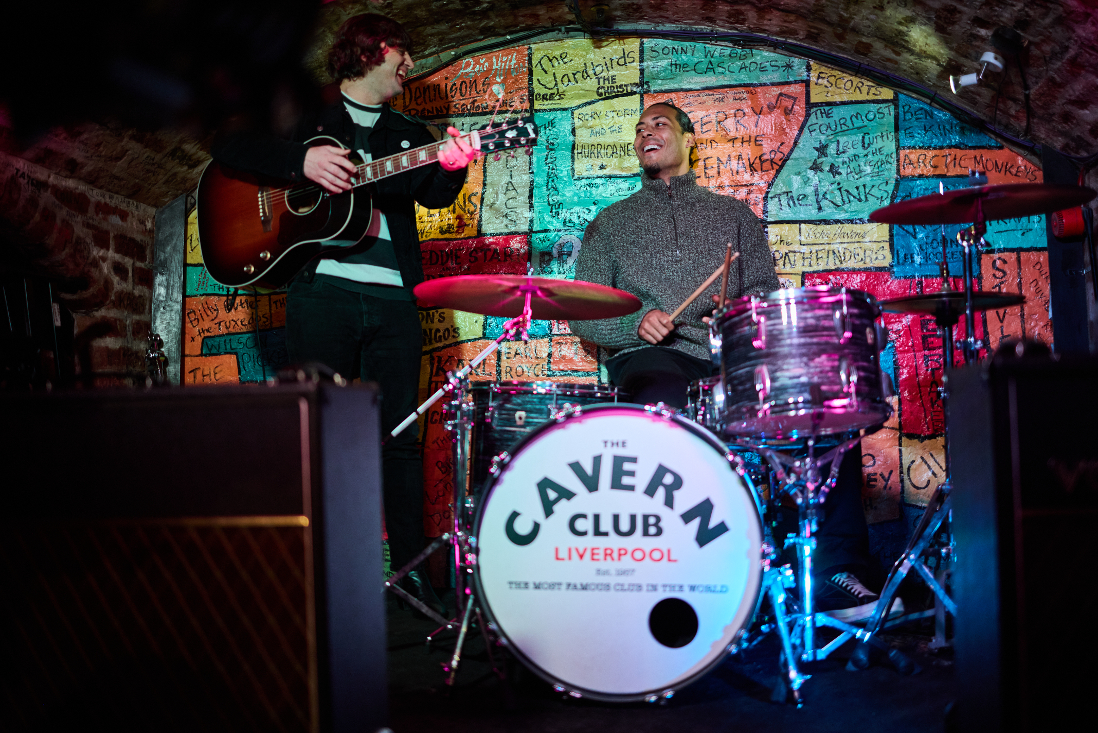 Musicians performing at The Cavern Club in Liverpool, with iconic logo drum set in the foreground