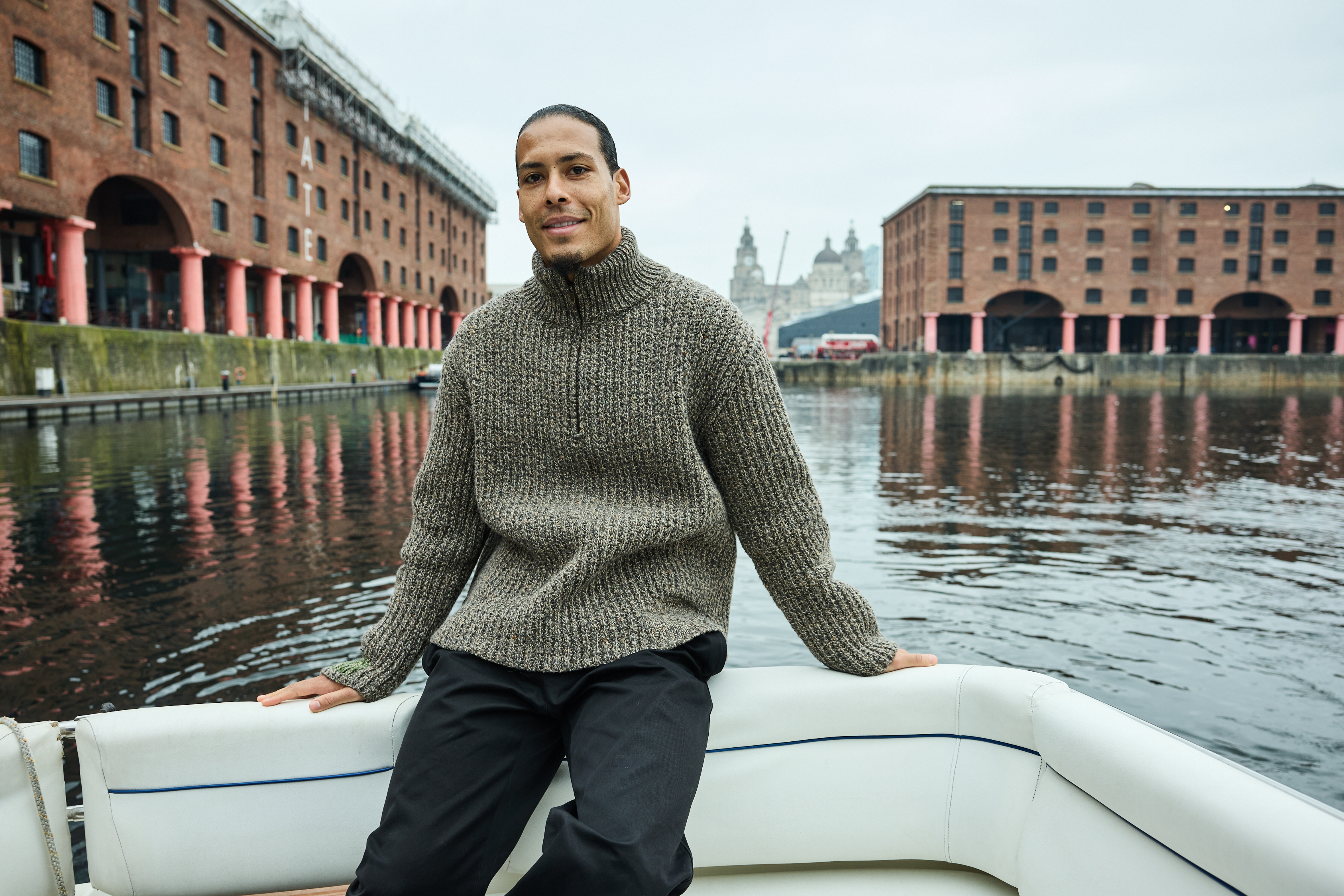 Man in a sweater seated on a boat with historical buildings in the background