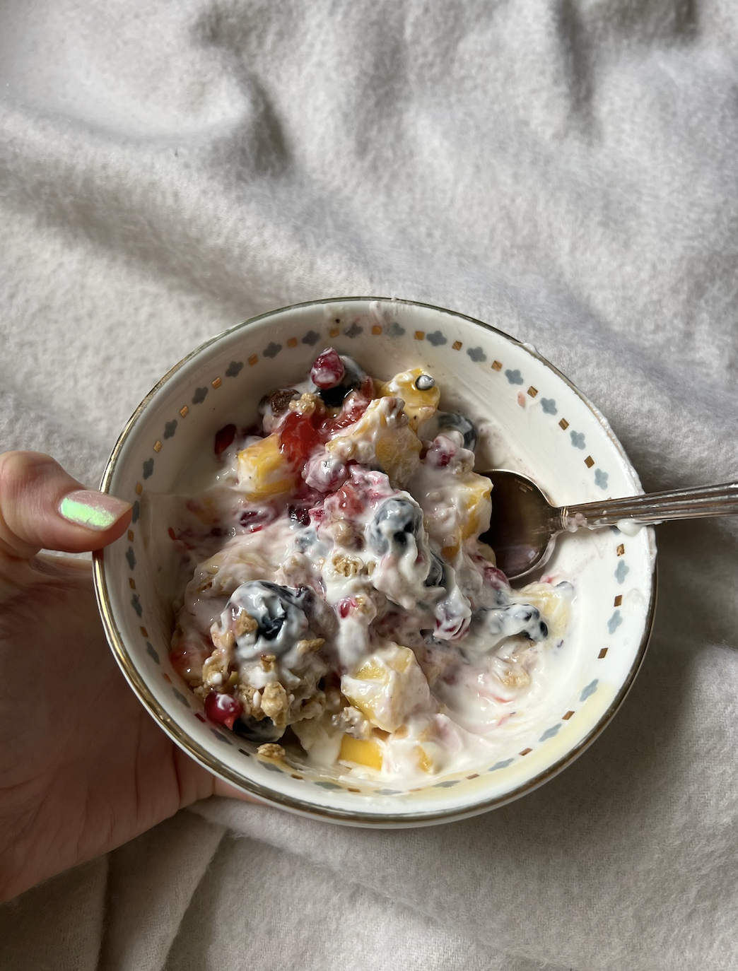 Person holding a bowl of mixed fruit and yogurt with a spoon, from a first-person perspective