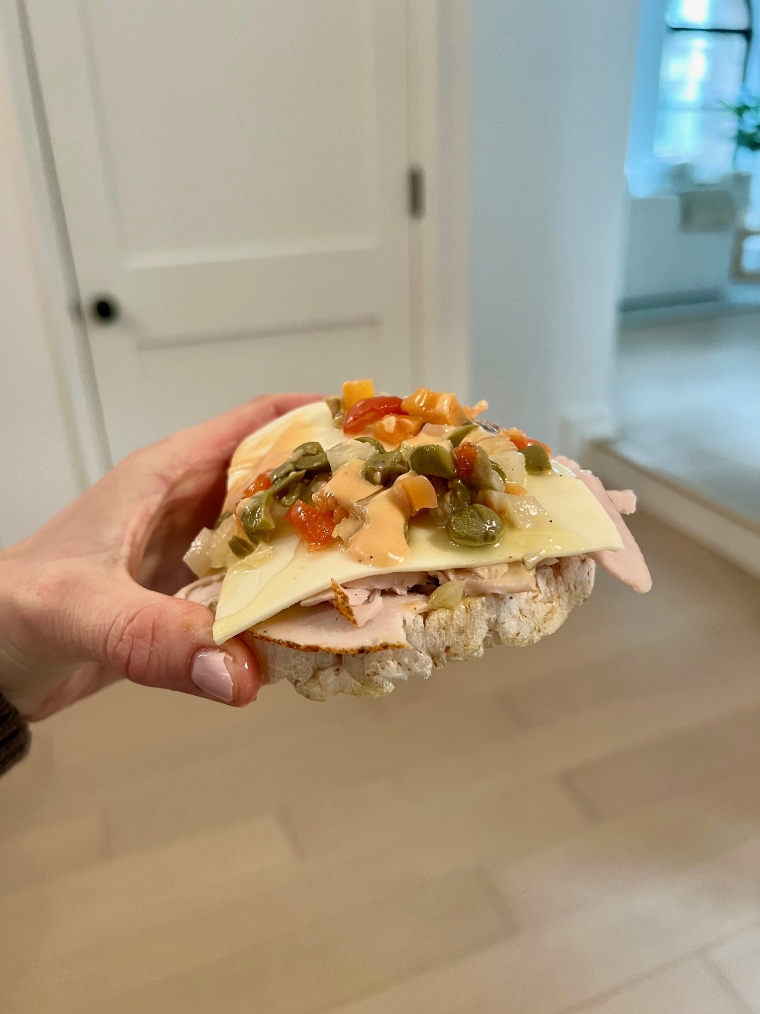 Hand holding a sandwich with turkey, cheese, and pickled vegetables