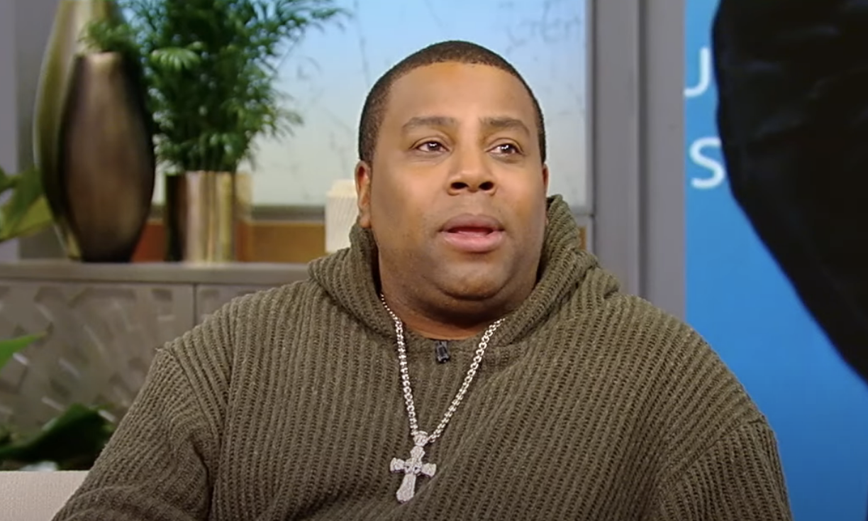 Kenan Thompson wearing a brown sweater and a cross necklace during an interview