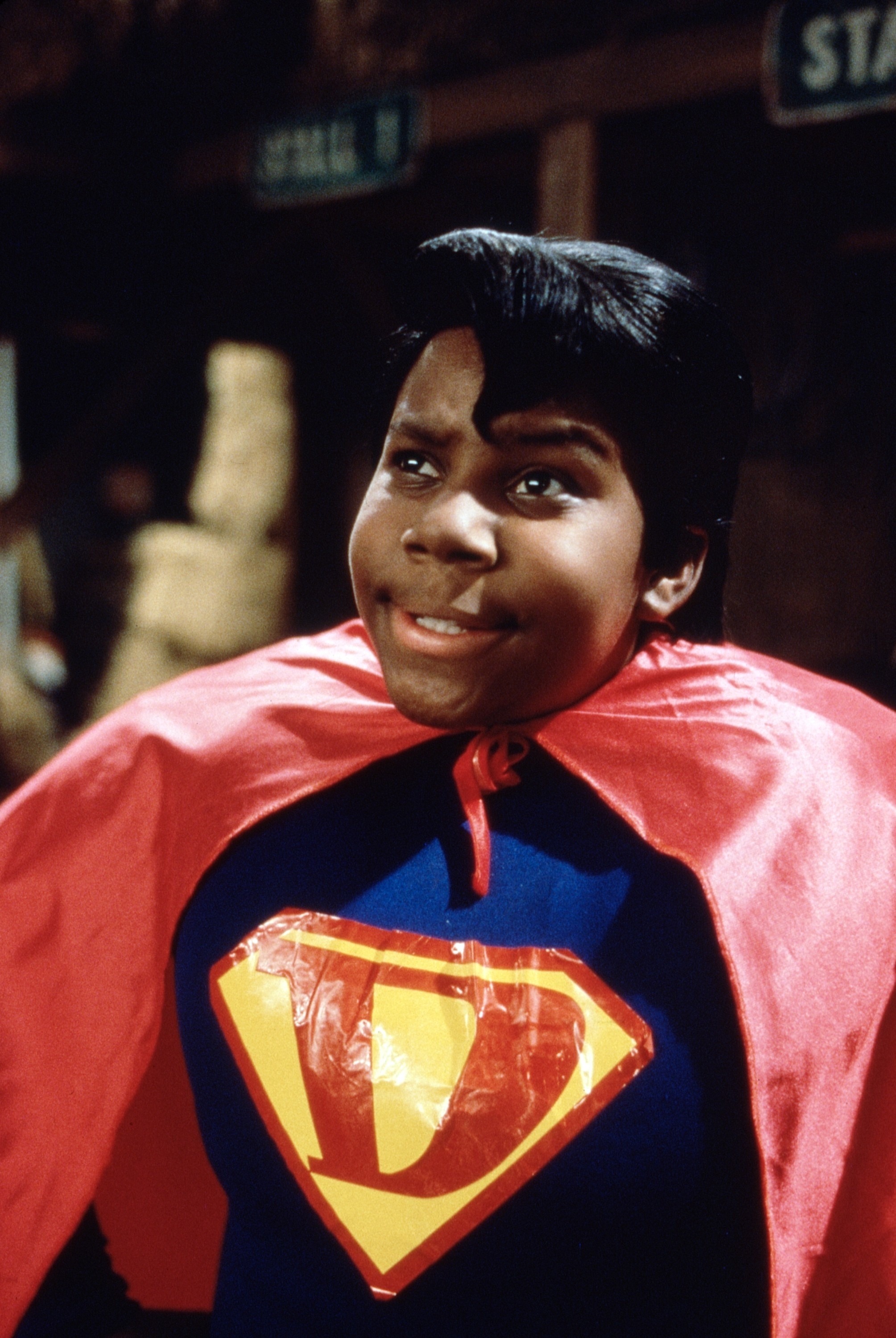 Kenan Thompson dressed as a superhero with a cape and a parody Superman logo on his chest