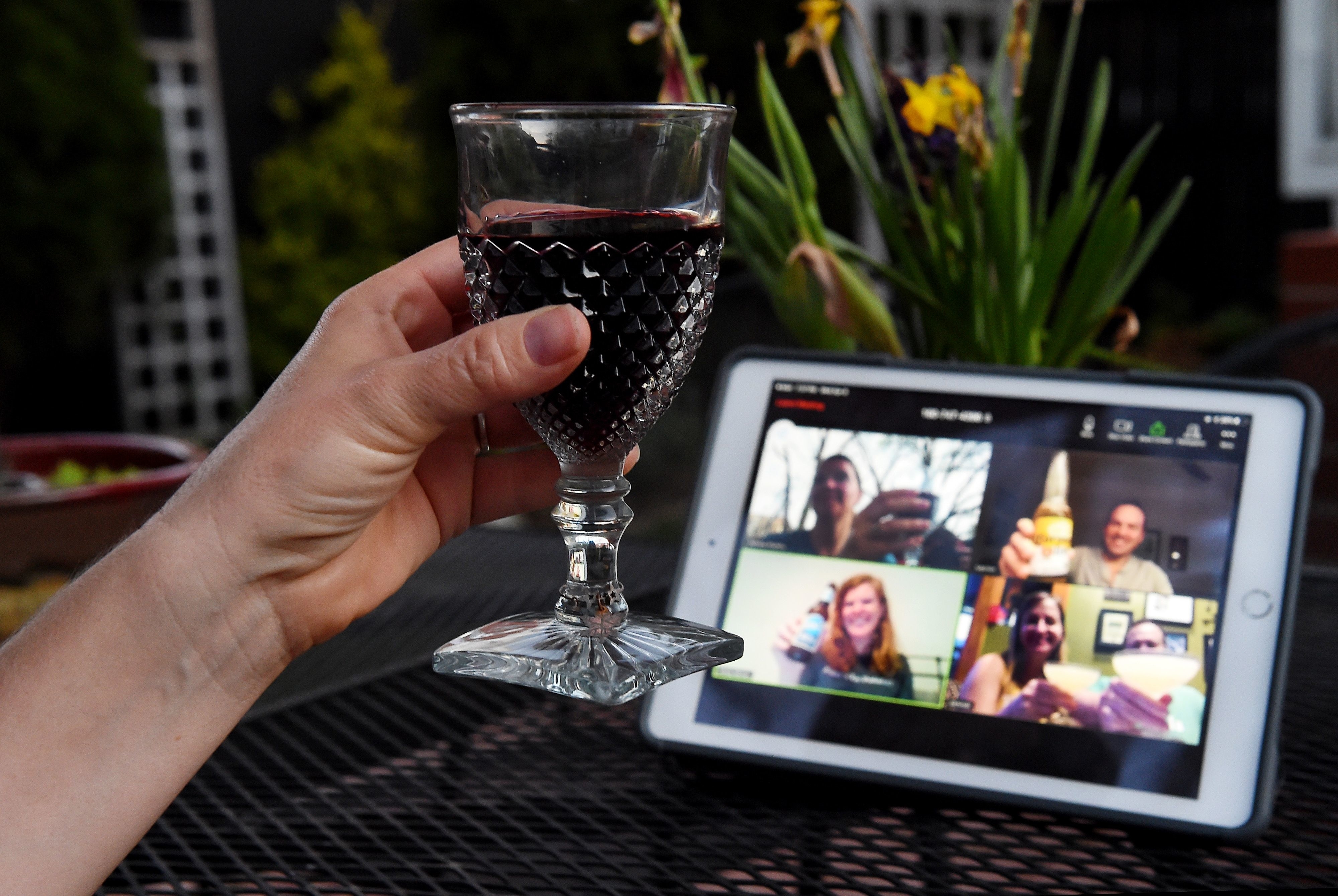 Person raising a glass in a virtual toast with friends on a tablet screen