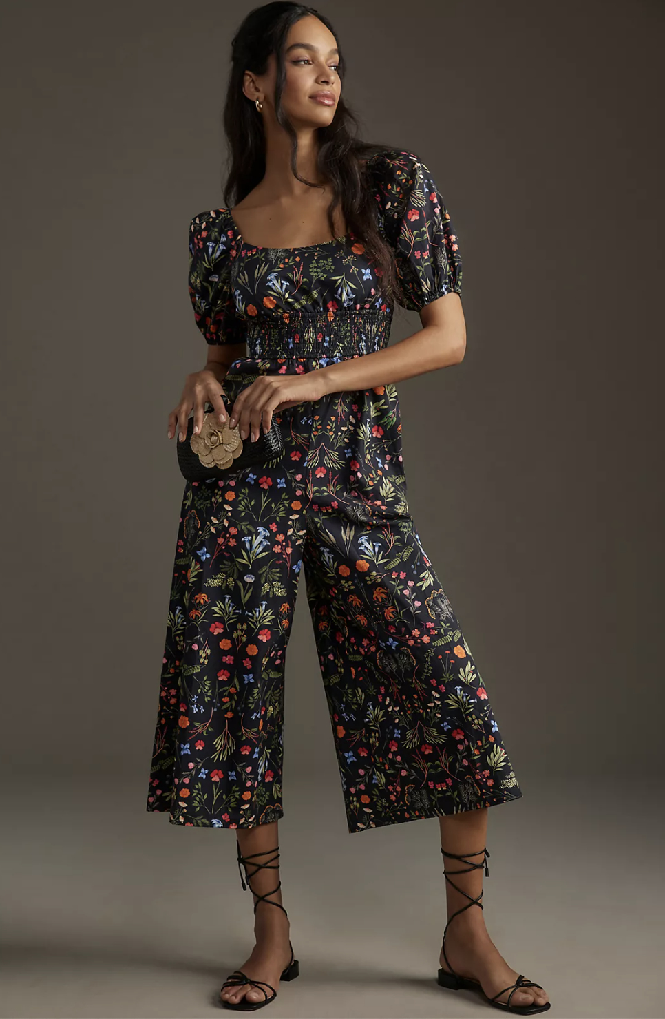 Woman in floral cropped top and culottes holding a small purse, standing in a model pose