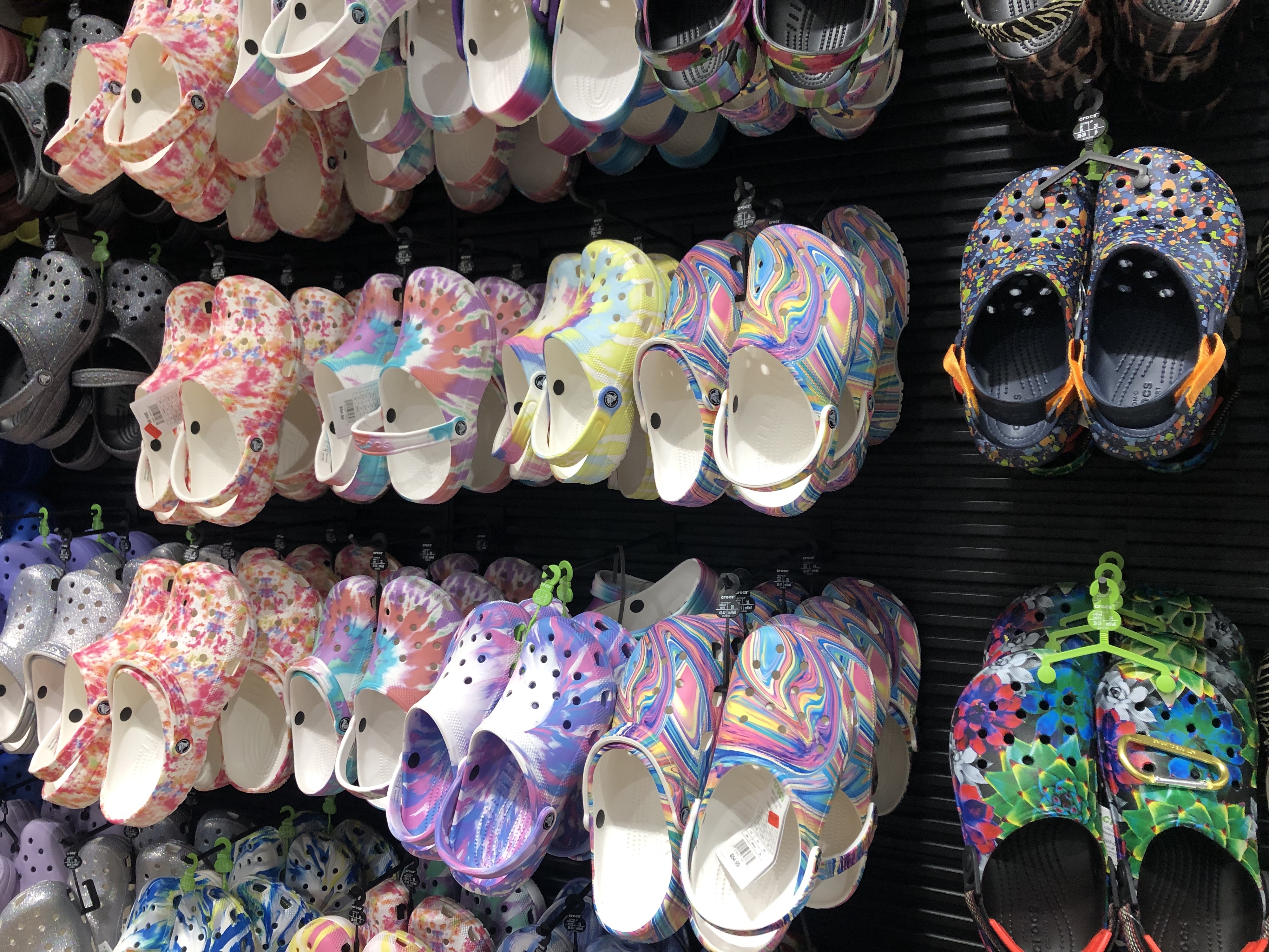 An assortment of various styles of Crocs footwear displayed on a retail store rack