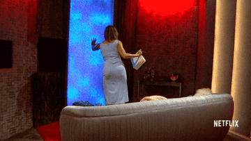 Woman in elegant dress touches interactive wall on set, Netflix logo visible