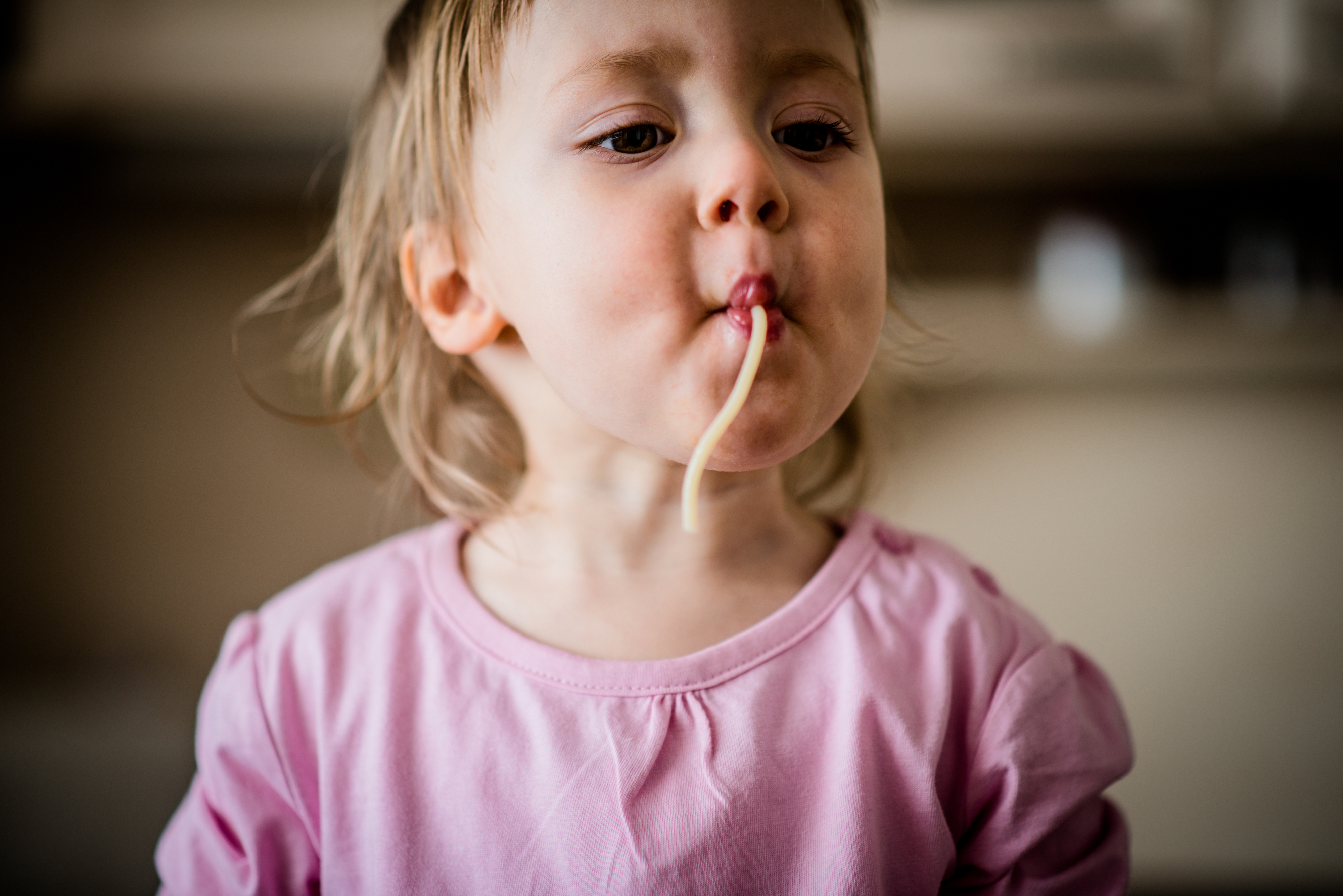 A child in a pink shirt focusing on eating a strand of spaghetti