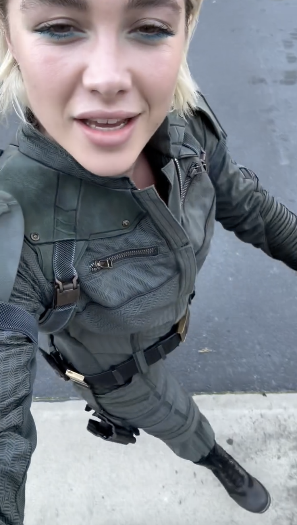 Florence Pugh in a tactical outfit with harness, taking a selfie