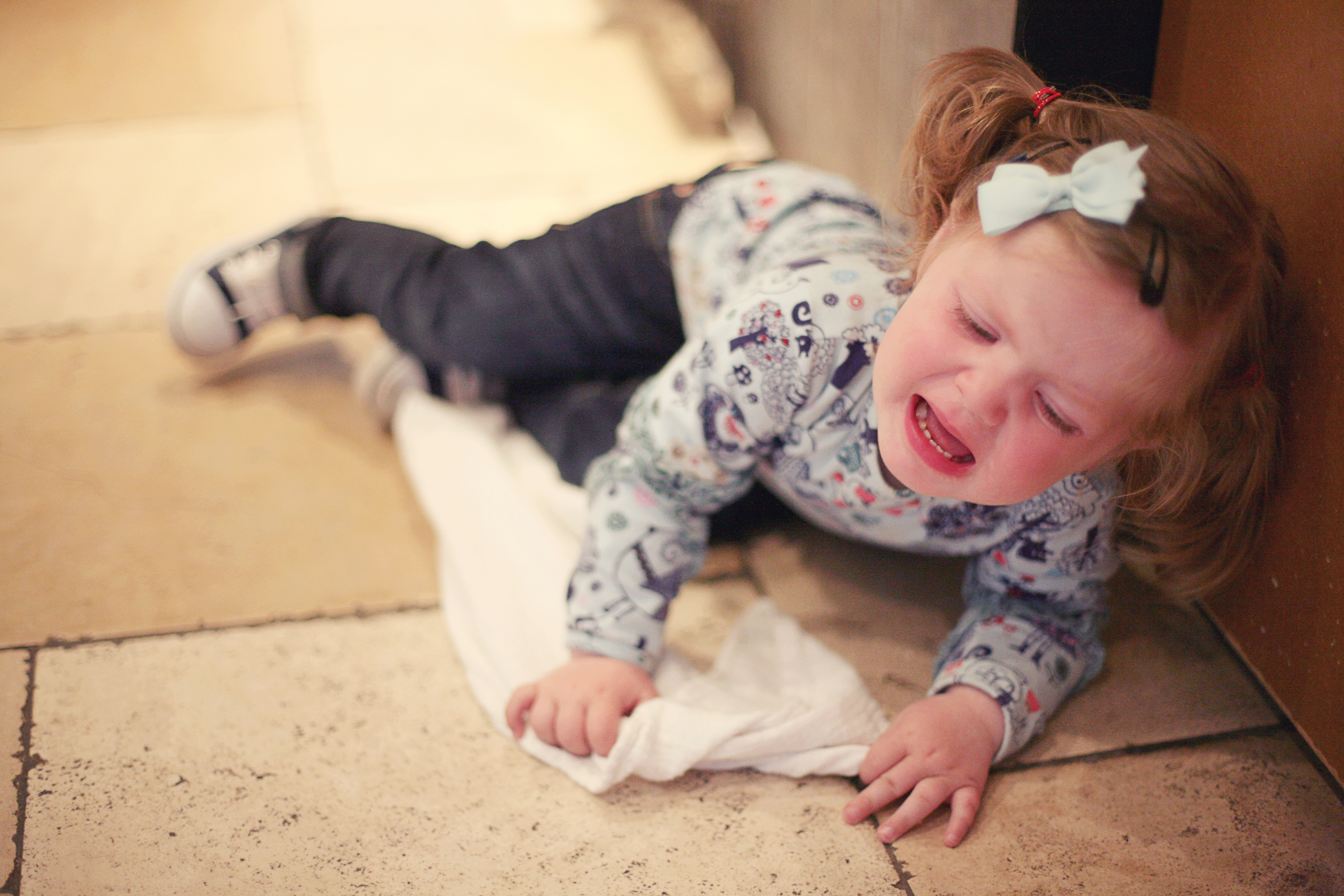 Toddler lying on the floor crying, wearing a patterned top and bow in hair